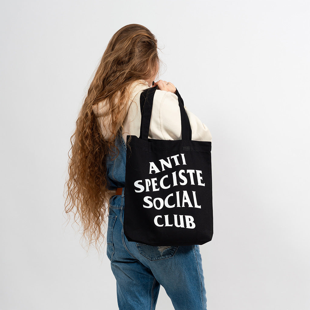 Mannequin femme de dos portant le tote bag noir avec sérigraphie blanche Anti Spéciste Social Club à l'épaule.