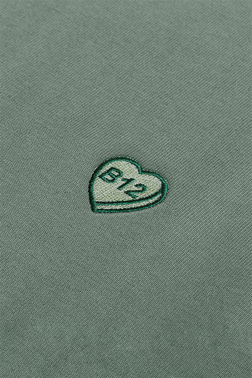 Détail de la broderie verte en forme de comprimé de B12 en coeur.