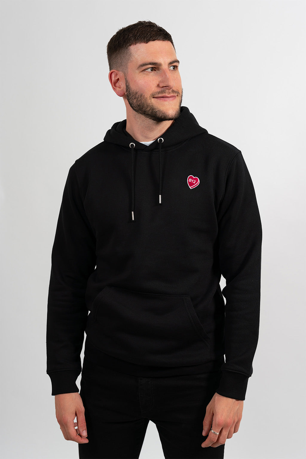 Mannequin homme portant un hoodie noir avec une broderie fuchsia en forme de comprimé de B12 en coeur.