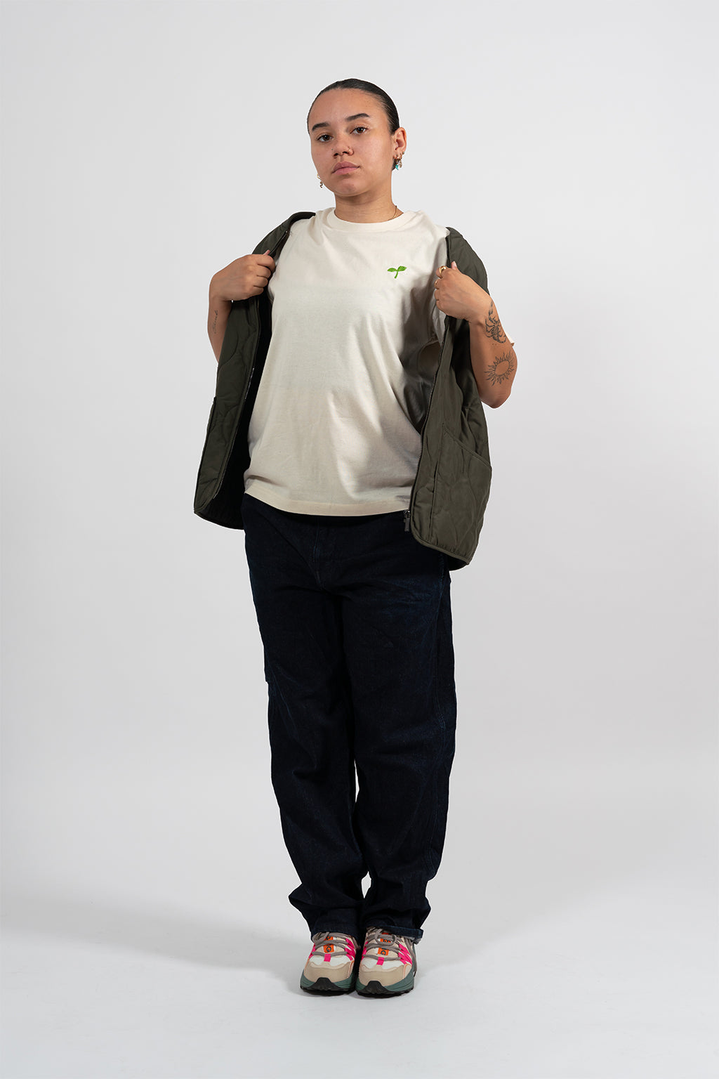 Mannequin femme portant un t-shirt beige avec une broderie verte représentant un Emoji Pousse.