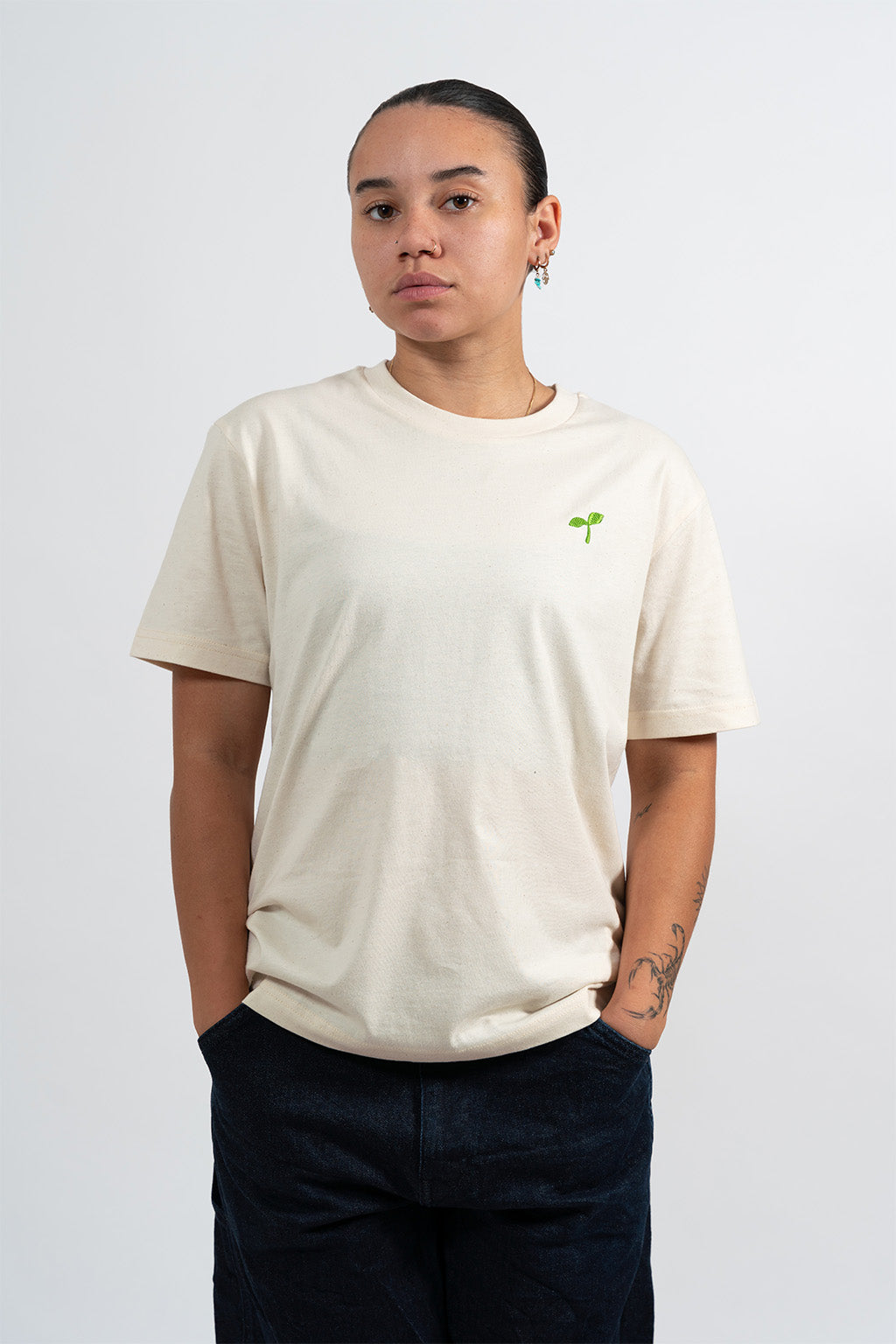 Mannequin femme portant un t-shirt beige avec une broderie verte représentant un Emoji Pousse.