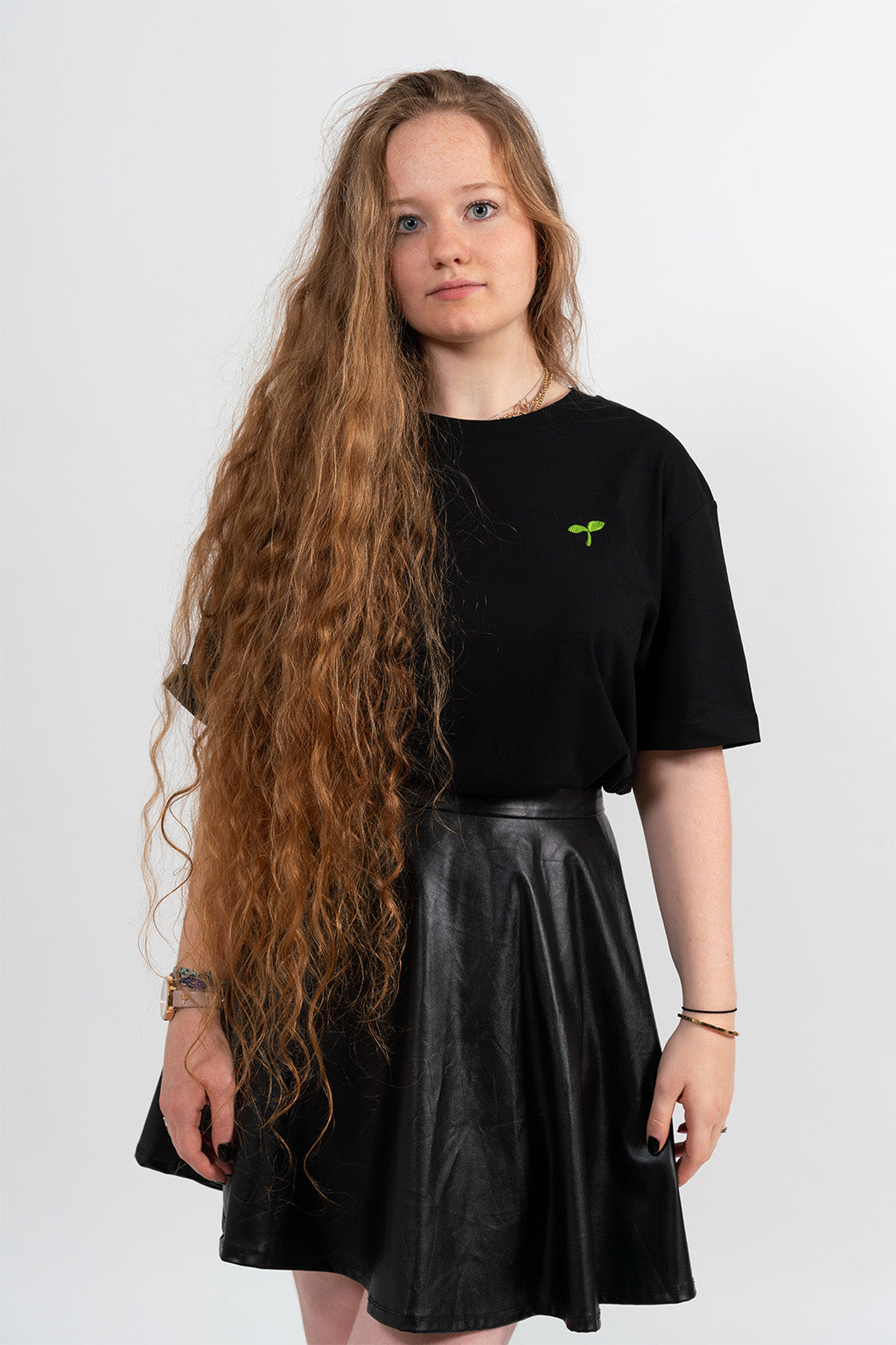 Mannequin femme portant un t-shirt noir avec une broderie verte représentant un Emoji Pousse.